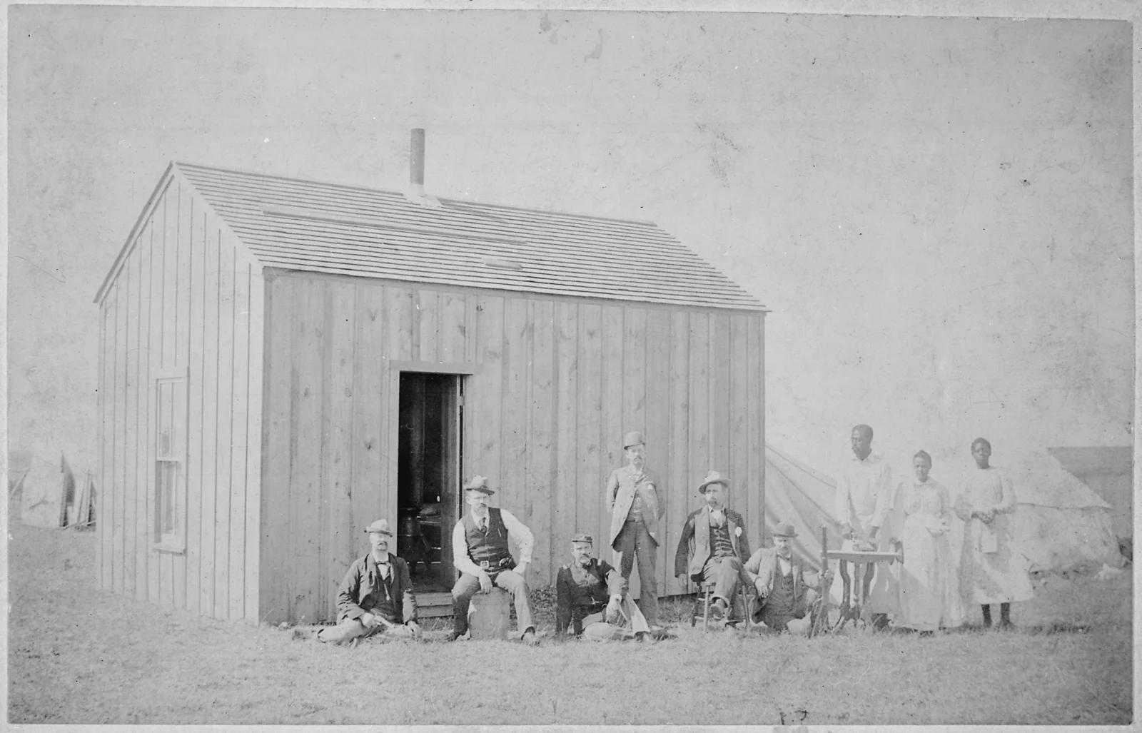 1893 photograph: the wooden shack of W. H. McCoy's homestead claim in Perry, Oklahoma Territory, with a group of people posing by the entrance.
