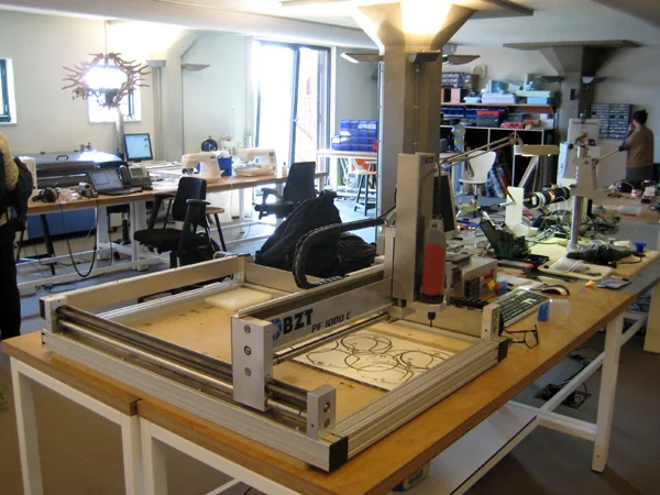 Interno di un Fab Lab: banchi di lavoro con attrezzature per la fabbricazione digitale e una persona impegnata sullo sfondo.
