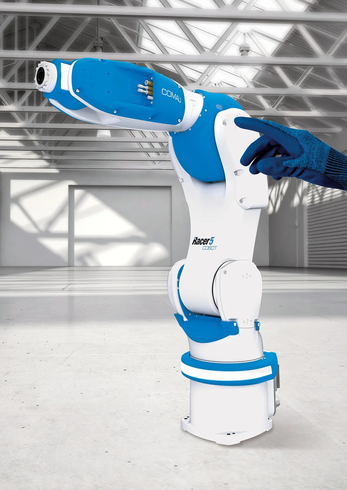 Braccio robotico collaborativo Comau Racer-5, bianco e azzurro, toccato da una mano con guanto blu in un capannone industriale luminoso.