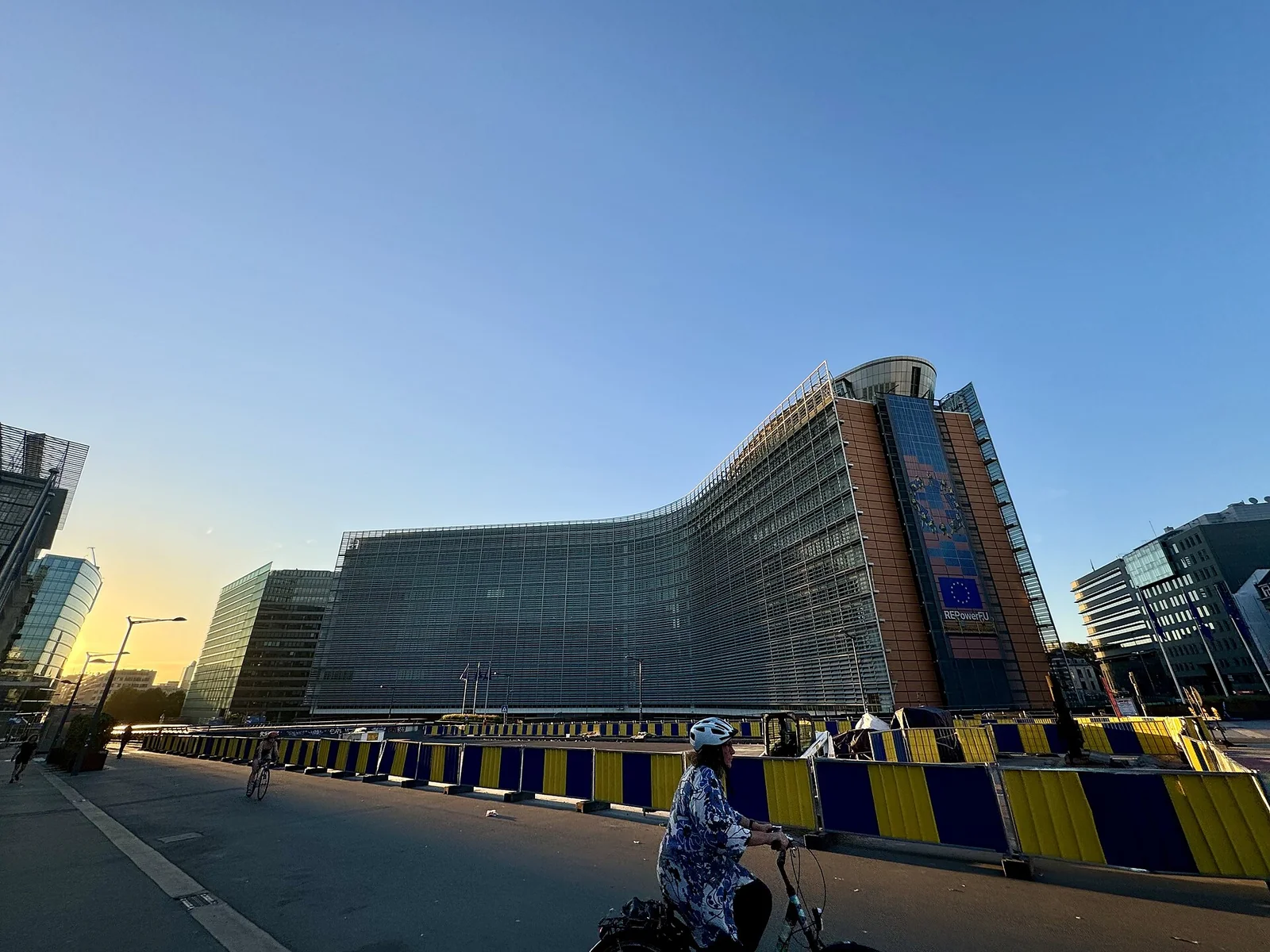 Il palazzo Berlaymont, sede della Commissione europea a Bruxelles, con le bandiere blu dell'Unione europea schierate davanti alla facciata curva in vetro.