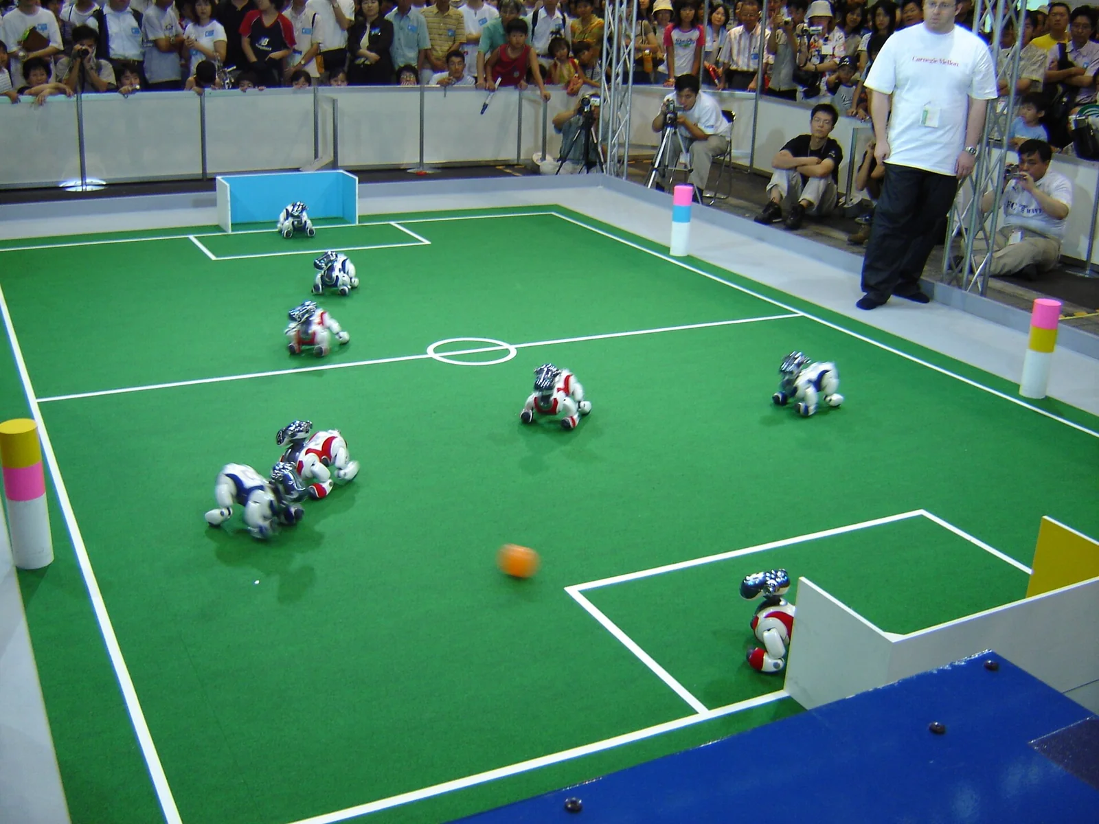 Diversi robot-cane Sony AIBO ERS-7 disposti su un campo verde mentre giocano a calcio durante una competizione robotica.