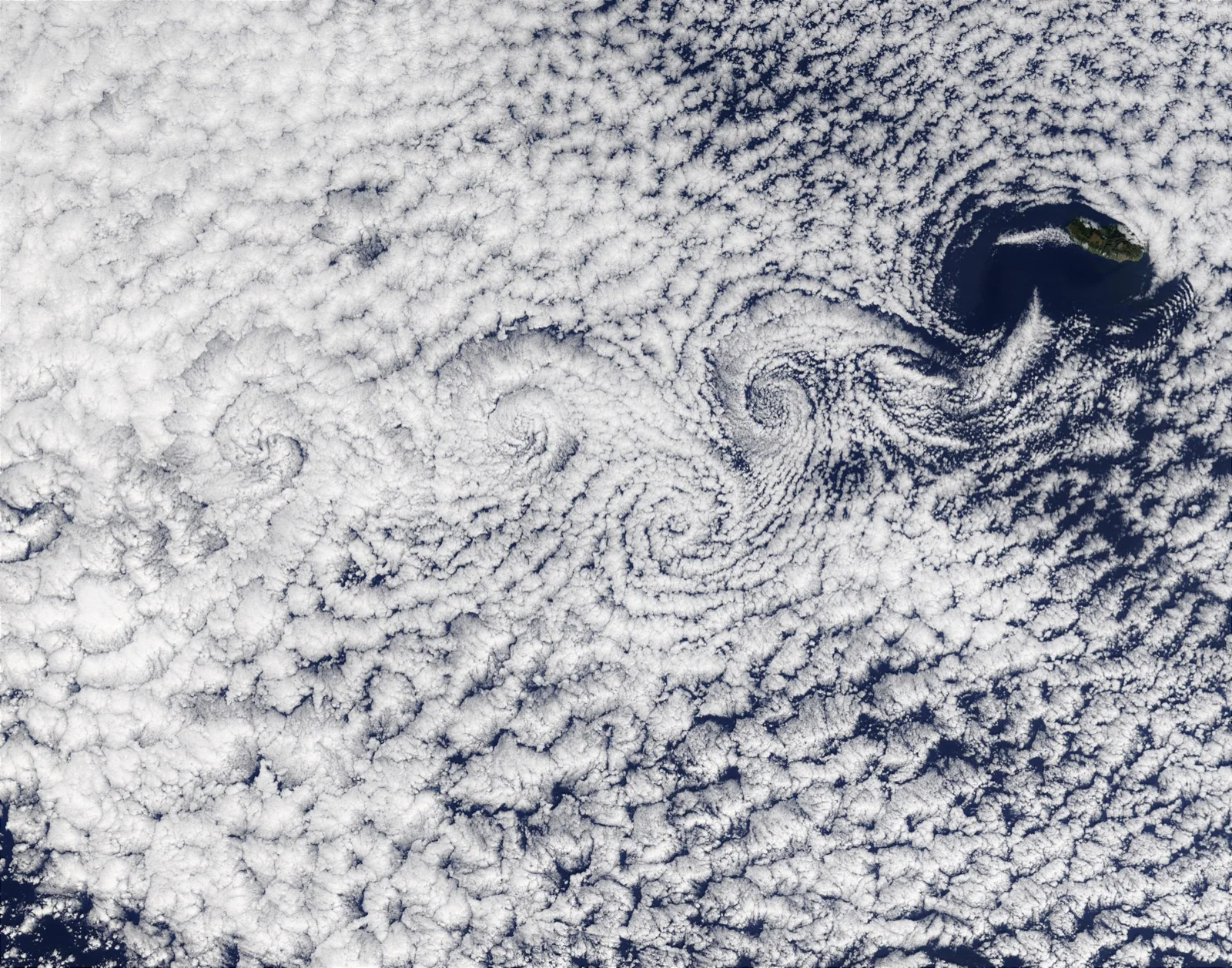 Immagine satellitare a colori naturali dell'oceano a sudovest di Madeira. Le nuvole basse formano una scia di vortici alternati che si avvitano l'uno dopo l'altro sottovento all'isola, visibile in alto a destra sul mare blu scuro.