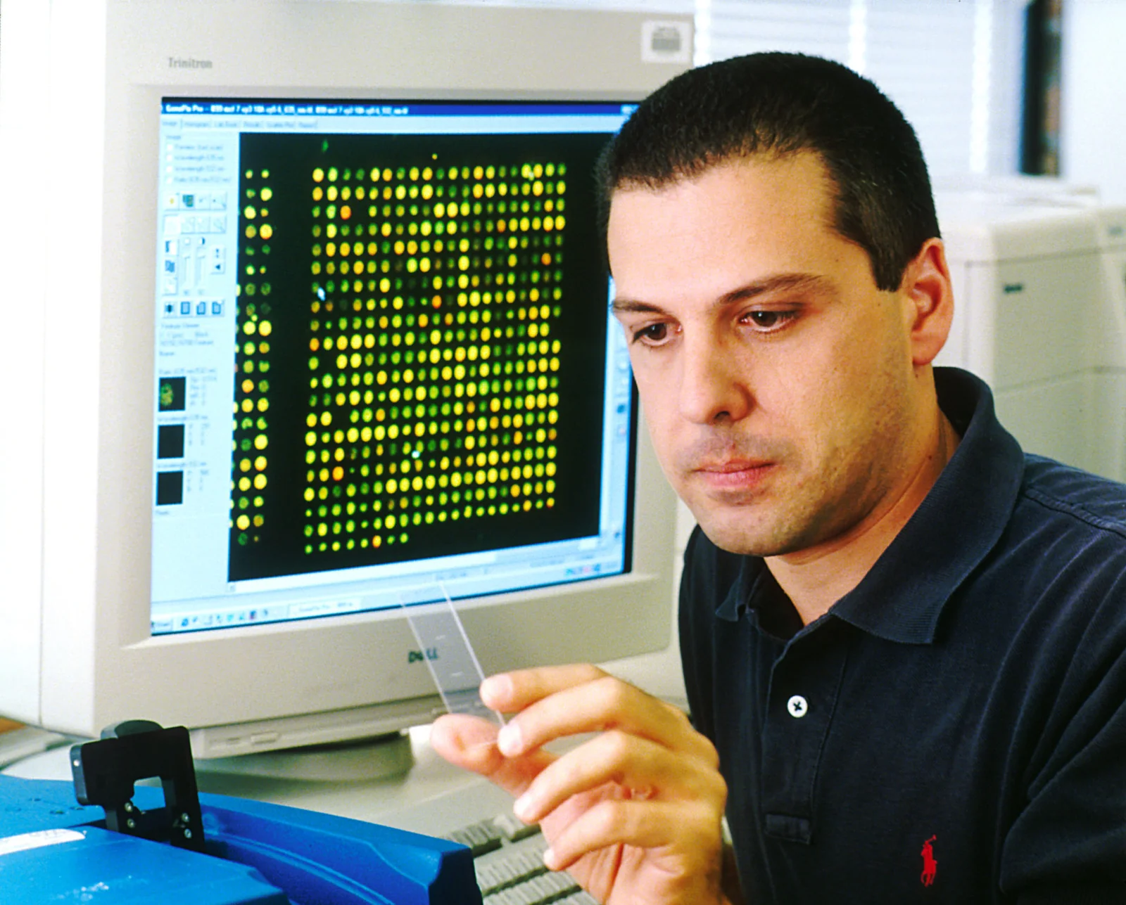 Tecnico di laboratorio seduto a un computer che mostra sullo schermo la griglia colorata di un microarray di DNA.