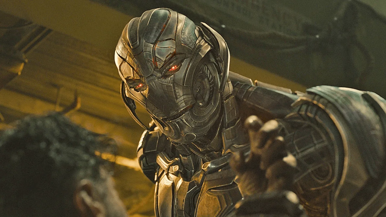 Ultron in Avengers: Age of Ultron. Testa e busto di un automa in metallo brunito, con il volto dalle placche sovrapposte inclinato in avanti e gli occhi rossi accesi, in una hangar dalla luce gialla.