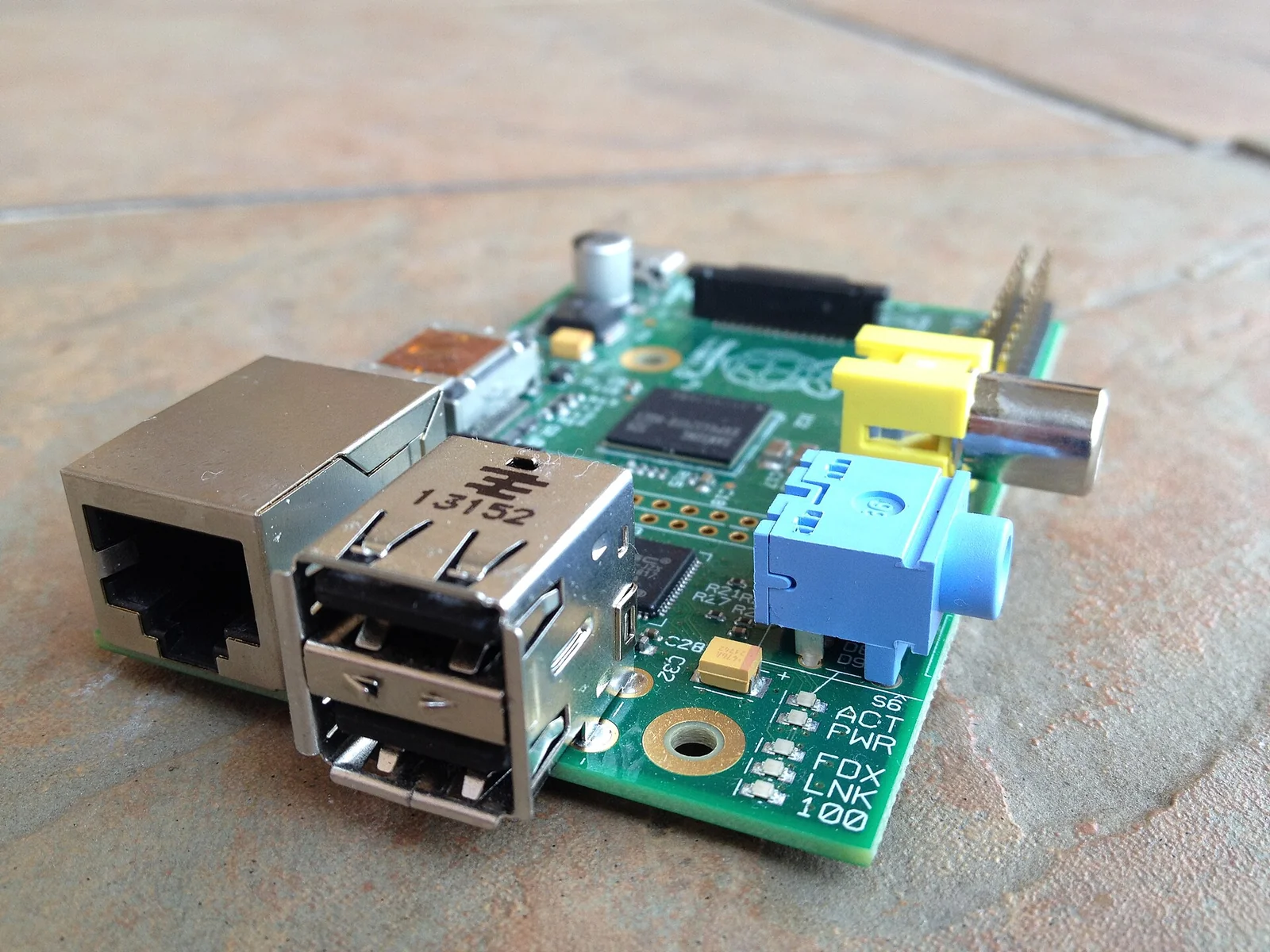 Scheda Raspberry Pi 1 Model B vista dall'alto su un piano chiaro: il circuito stampato verde con il SoC Broadcom centrale, due porte USB, la porta Ethernet, l'uscita HDMI, lo slot SD e l'header dei pin GPIO sul bordo.
