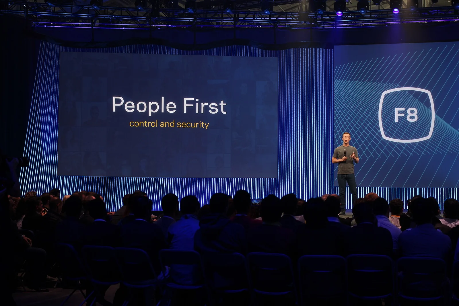 Mark Zuckerberg, in maglietta scura, parla sul palco illuminato della conferenza Facebook F8 2015 davanti a un grande schermo.