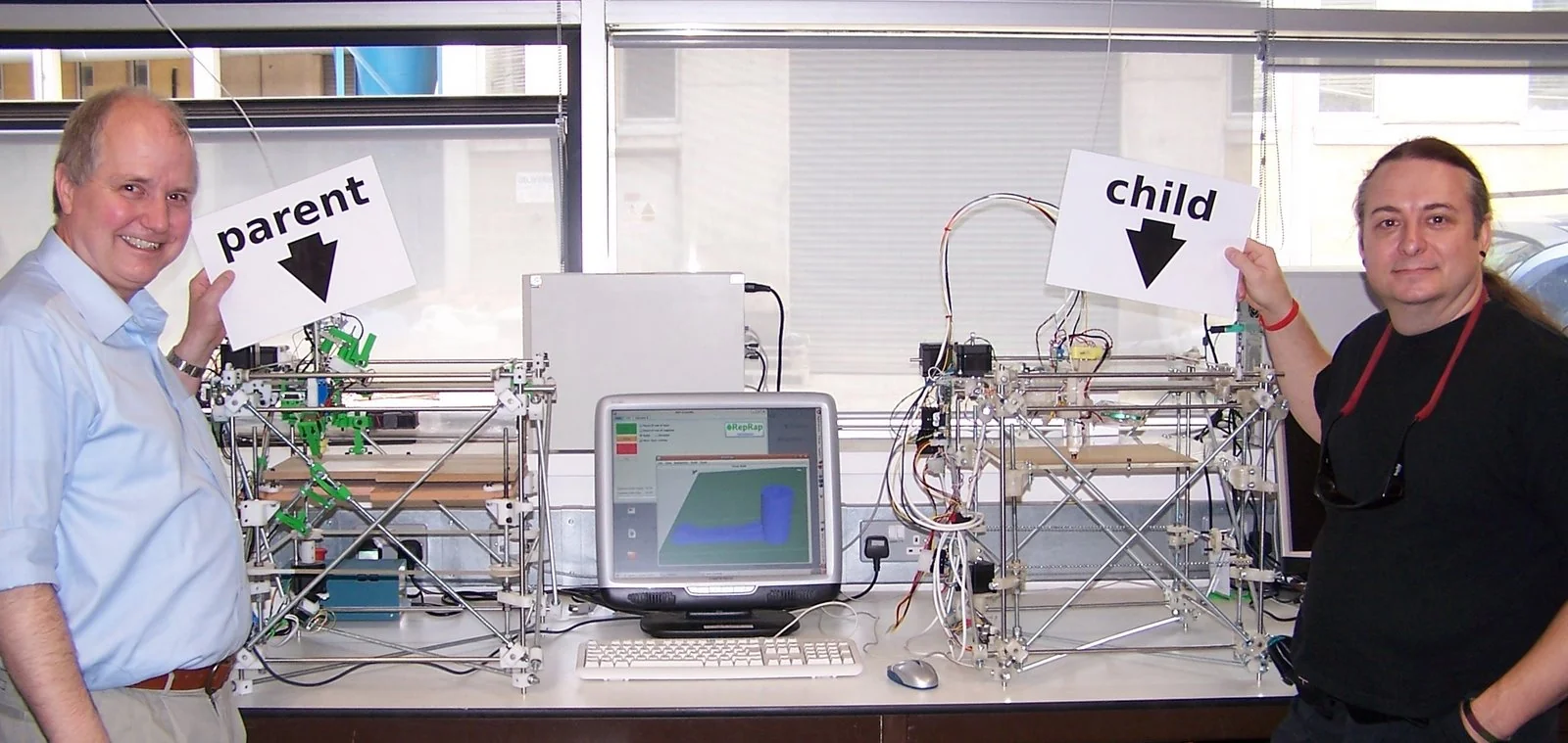 Adrian Bowyer, fondatore di RepRap, e Vik Olliver con due macchine RepRap Darwin: a sinistra la 'genitore', a destra la prima RepRap da essa prodotta.