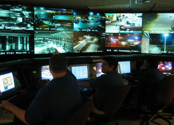 Due operatori seduti davanti a una parete di monitor in un Security Operations Center, con dashboard e grafici di rete sugli schermi.