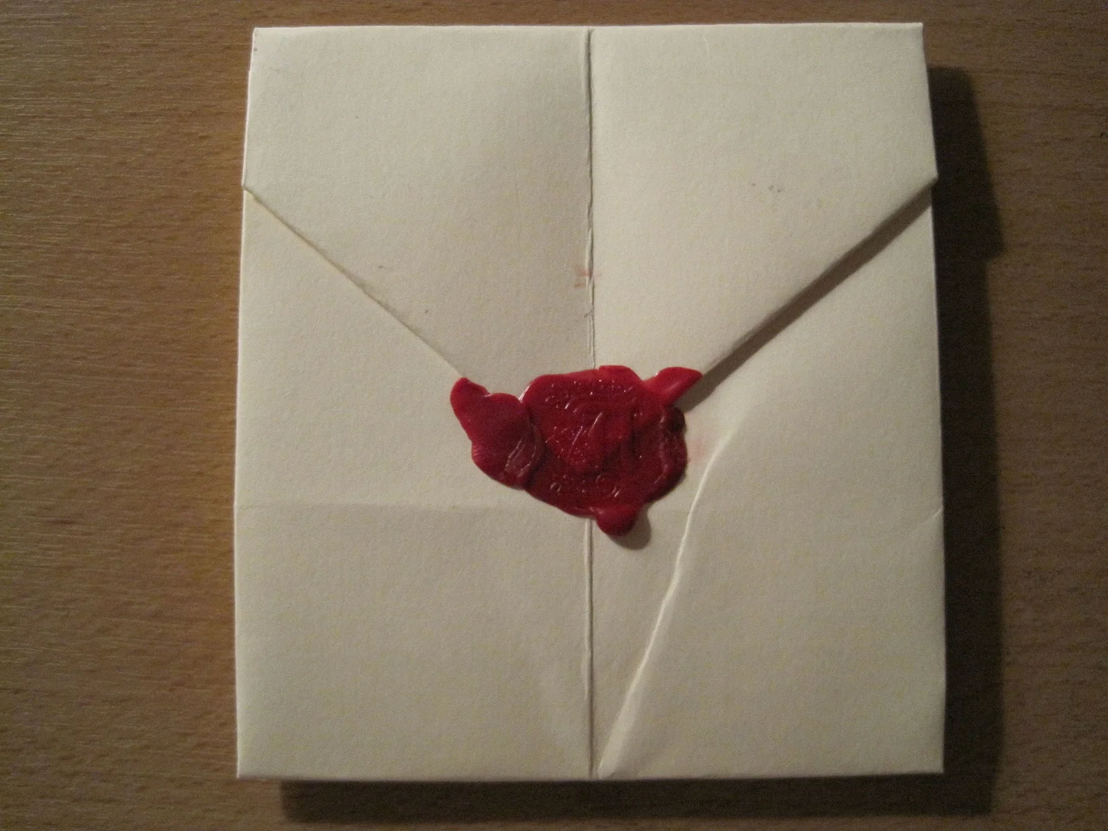Lettera di carta piegata a mano, chiusa da un sigillo di ceralacca rossa con impressa la lettera 'A'.
