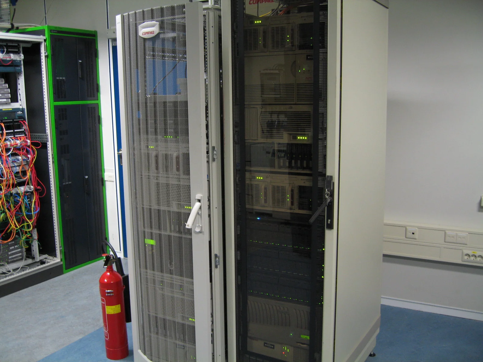 Rack metallico pieno di server Compaq impilati con cavi e un array di storage NAS in una sala macchine.