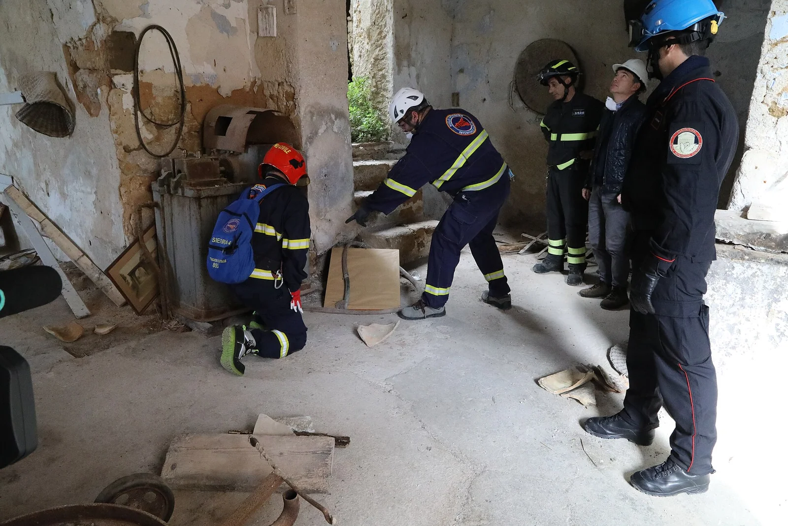 Squadra di soccorritori della protezione civile, con caschi ed elmetti e divise ad alta visibilità, durante una ricognizione all'interno di un edificio danneggiato in un'esercitazione di maxi-emergenza.