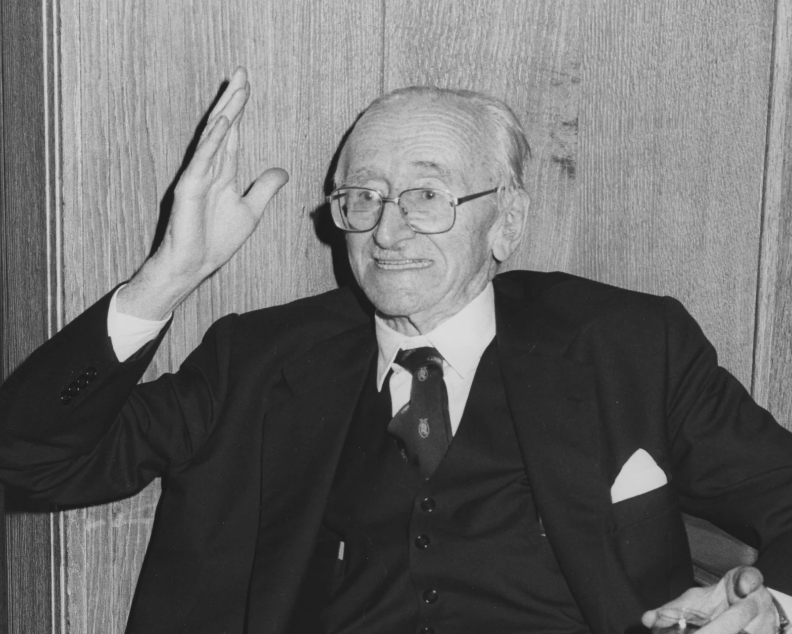 Ritratto in bianco e nero di Friedrich Hayek anziano, in abito con panciotto, la mano destra alzata mentre parla (1981).